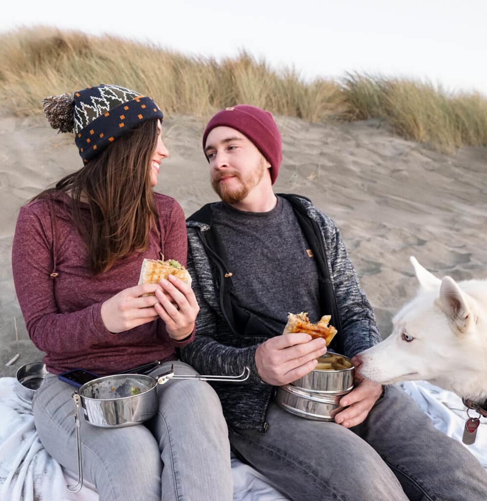 A man, woman, and their dog enjoying a lunch packed with their hiking gear essentials.