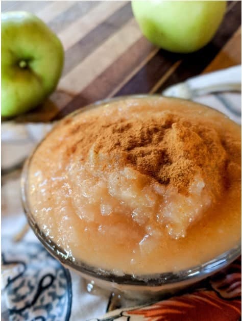 close-up image of a bowl of applesauce and green apples in the background